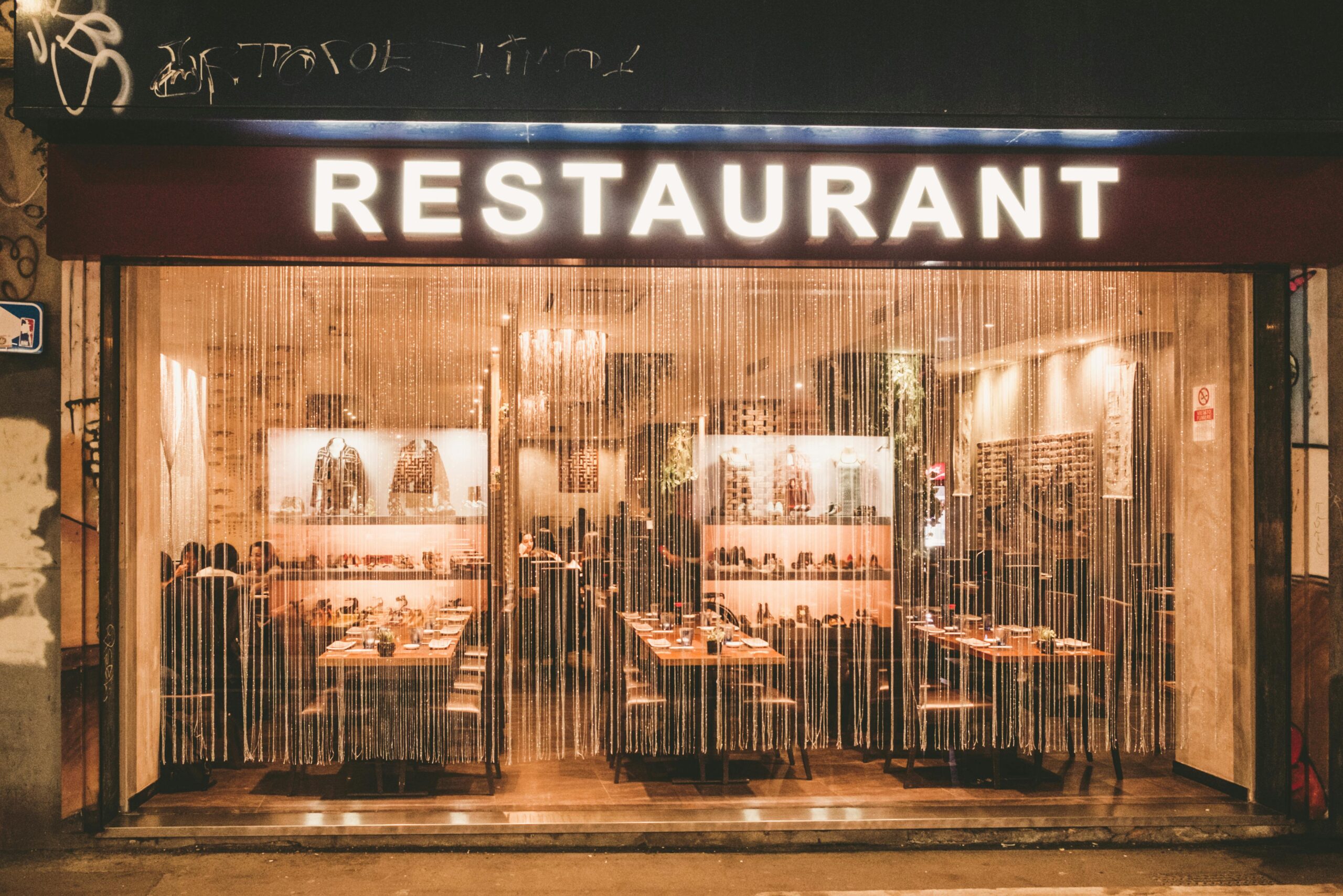 A warmly lit restaurant exterior on a street in Milan, Italy, featuring elegant decor and ambience.